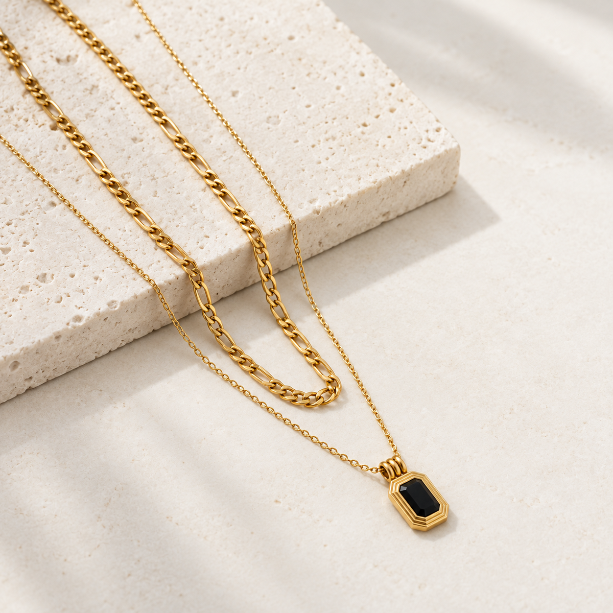 Gold-tone layered necklace with link chain and black rectangular pendant on white background
