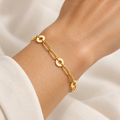 Gold-tone circle and textured elongated link bracelet laid on beige stone