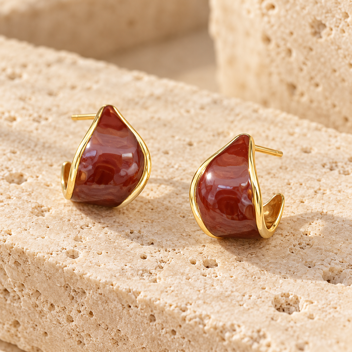 Pair of reddish-brown and gold-tone curved hoop earrings on white